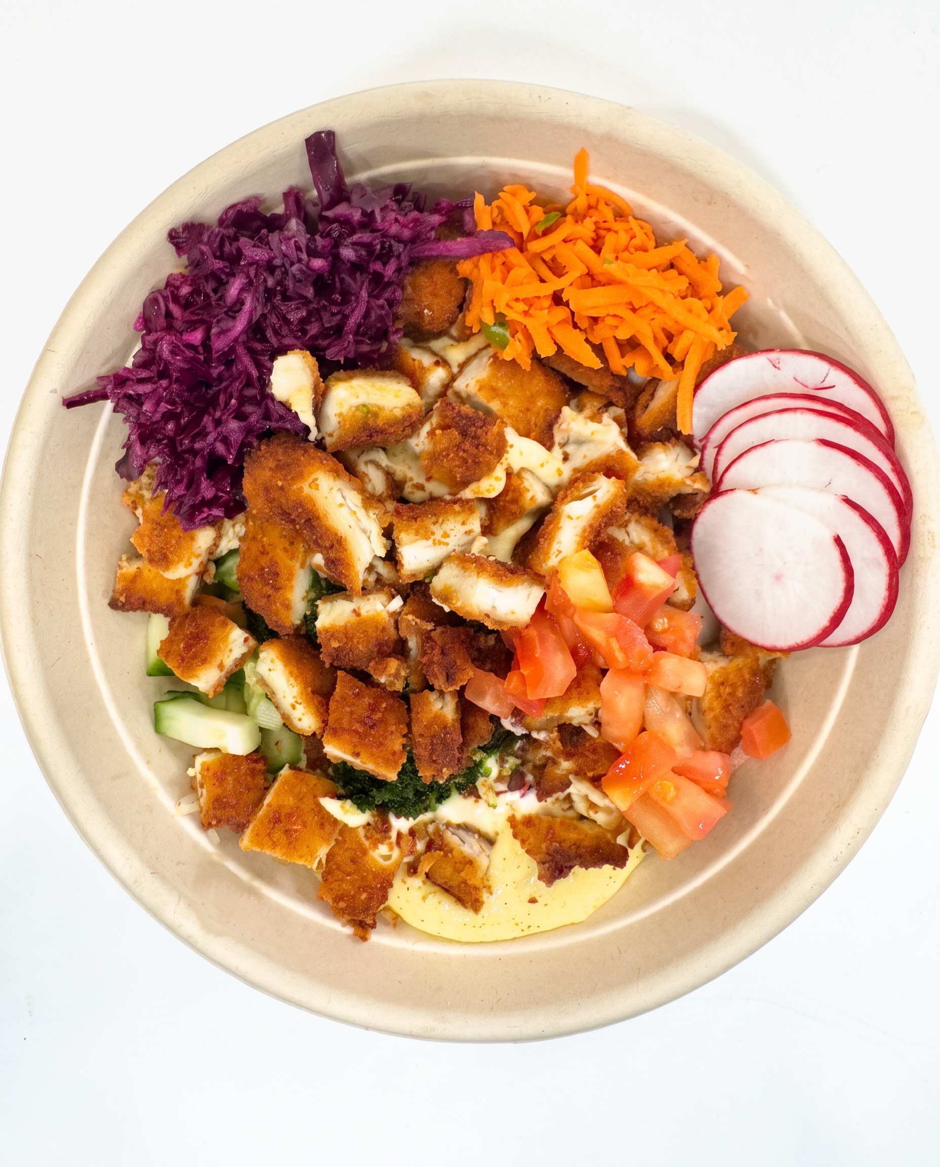 Overhead bowl of crispy chicken with red cabbage, shredded carrot, radish, tomato and hummus