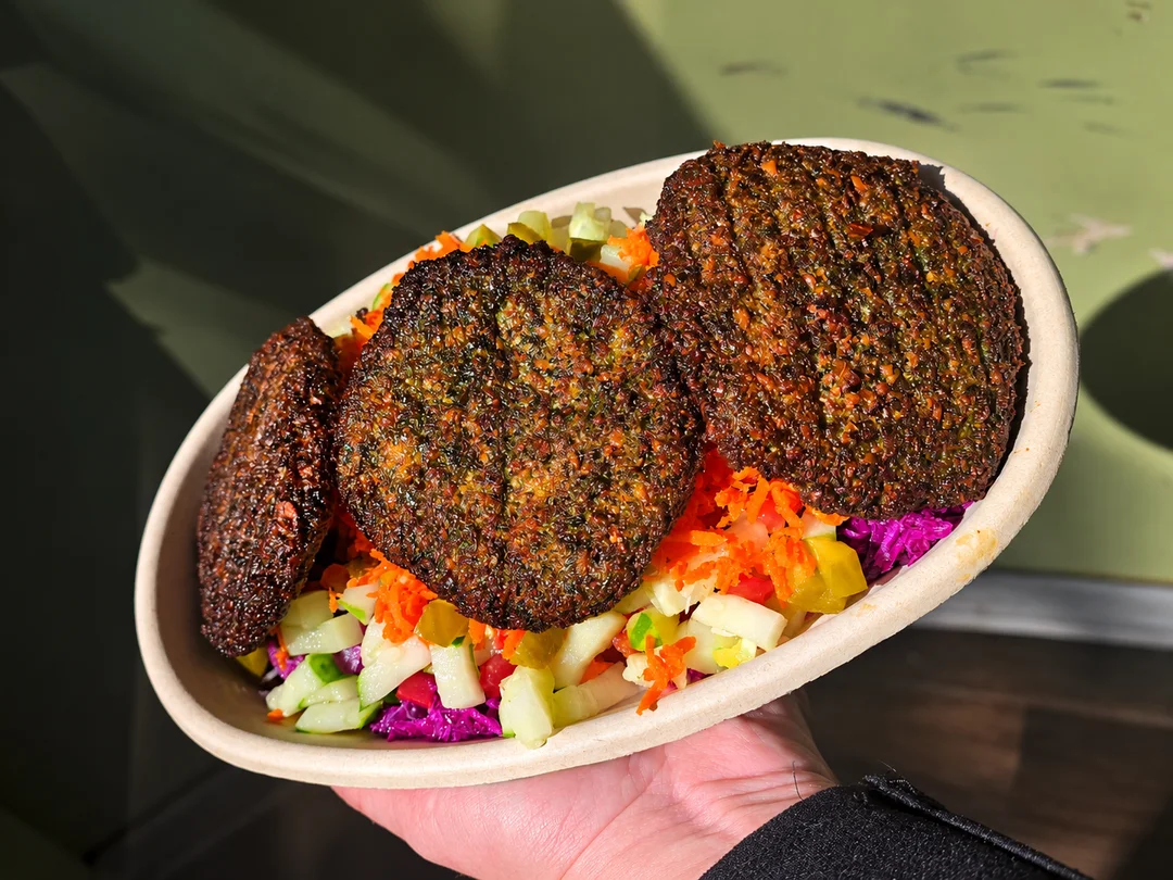Three crispy falafel patties over shredded carrots, cucumbers, tomatoes and purple cabbage in a bowl