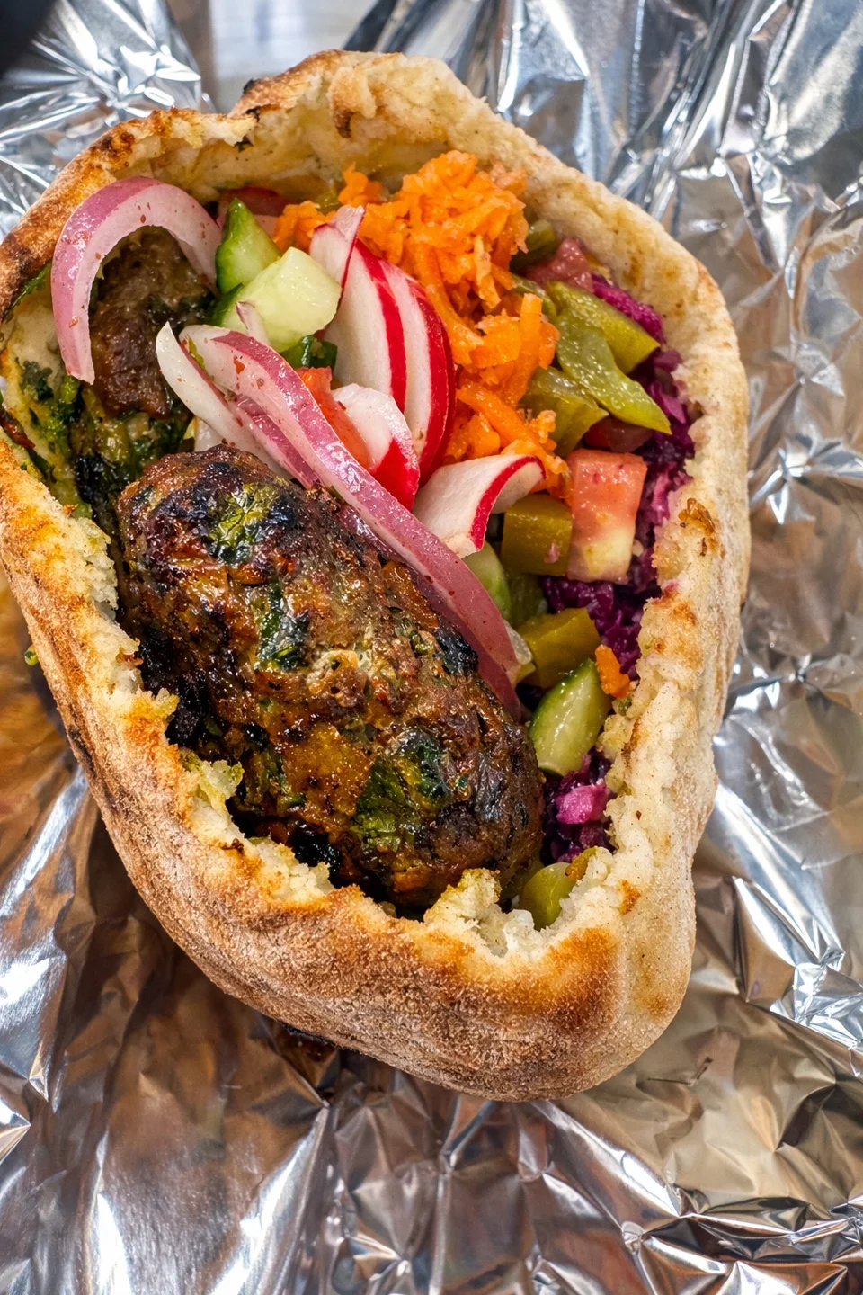 Pita stuffed with grilled kabob, purple cabbage, pickles, radish and pickled turnip on foil