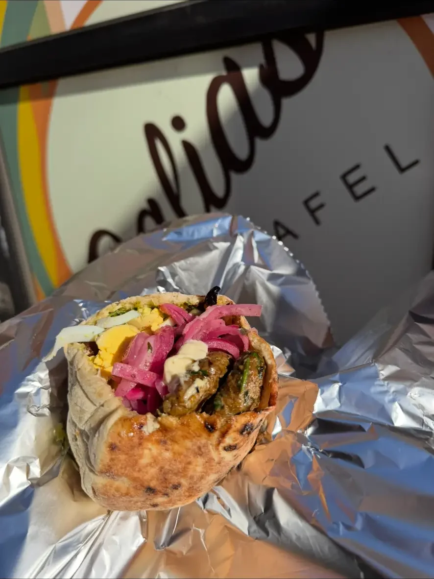 Kabob pita with pickled onions, egg and garlic sauce in front of the Dalia's Falafel sign
