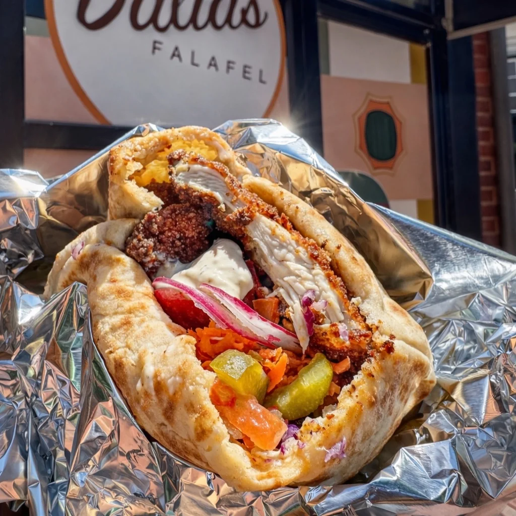 Chicken schnitzel pita held up in front of the Dalia's Falafel storefront sign